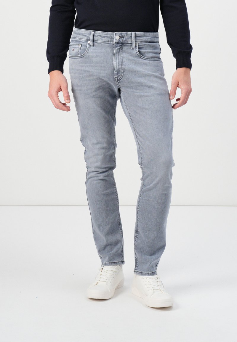 Light grey skinny jeans made from denim, featuring a classic five-pocket design and a subtle faded texture. Worn with white sneakers.