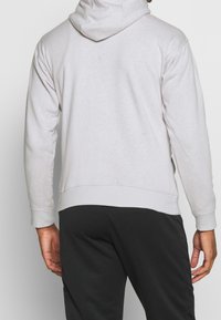 Světle šedá mikina s kapucí vyrobená z měkké tkaniny, s volným střihem a žebrovanými manžetami, spárovaná s černými tepláky.