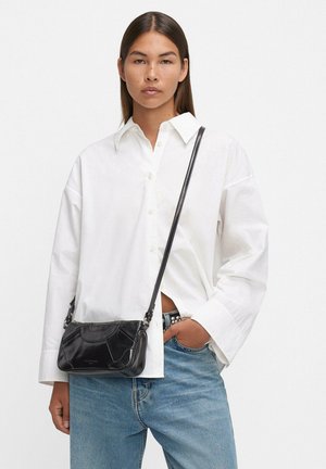 Borsa a tracolla in pelle nera con design curvo, dotata di chiusura con zip, tracolla regolabile e delicati dettagli di cucitura.
