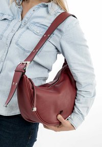 Red leather shoulder bag with a curved design, adjustable strap, and silver hardware accents. Zipper closure and smooth texture.