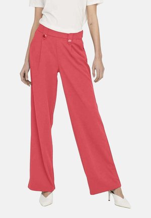 Pantalons corail à jambe large en tissu lisse ; dotés de deux boutons décoratifs à la taille ; accompagnés d'un haut blanc simple et de talons blancs.