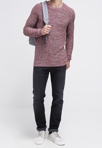 Rood en grijs gemêleerd gebreid sweater, ronde hals, gewone pasvorm, gecombineerd met donkere jeans en witte sneakers, aangevuld met een grijze rugzak.