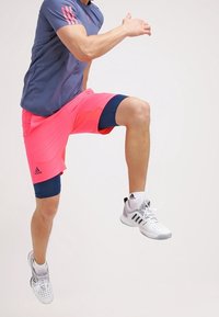 Conjunto deportivo que presenta una camiseta de manga corta en color azul marino y pantalones cortos rosa brillante con detalles en azul. Zapatillas deportivas compuestas en blanco y gris.