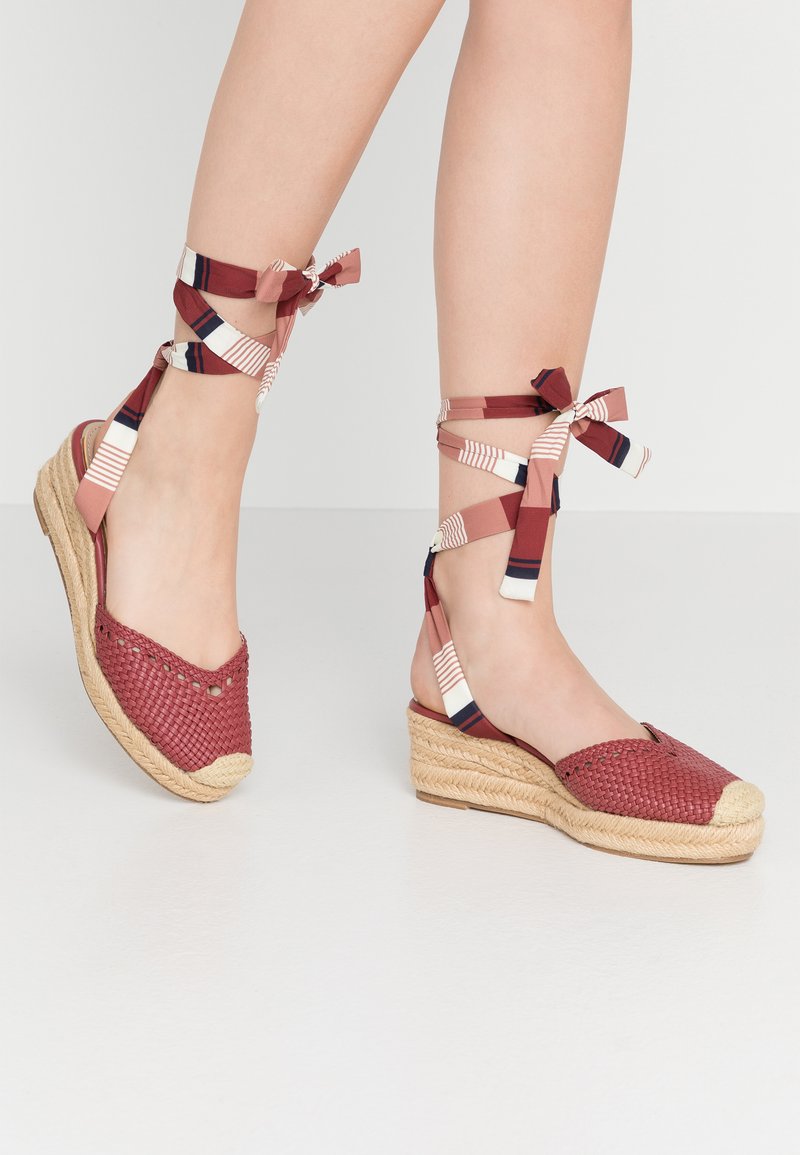 Rote gewebte Espadrilles mit einer natürlichen Jutesohle und Keilabsatz. Mit gemusterten Stoffriemen, die um den Knöchel gebunden sind. Offen vorne.
