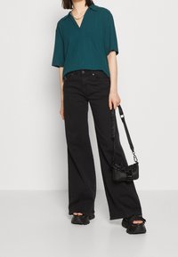 Teal ribbad kortärmad topp med krage, kombinerad med vida svarta jeans och en liten svart handväska med kedjehandtag. Åtsittande svarta skor.