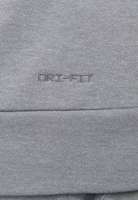 Szary materiał Dri-Fit o gładkiej strukturze, wyraźnym przeszyciu i haftowanym logo z napisem "DRI-FIT" na dole.