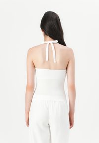 Bílý top s holými rameny vyrobený z hladkého materiálu, s krčním vázáním, přiléhavým korzátem a jemnou texturou. Pohled ze zadu ukazuje minimalistický design.