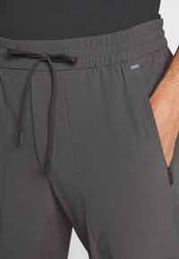 Ciemnoszare spodnie sportowe z elastyczną talią, regulowanym sznurkiem, boczną kieszenią na zamek oraz subtelnym, teksturowanym wykończeniem.