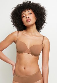 Reggiseno imbottito marrone con spalline regolabili, coppe senza cuciture e texture liscia, indossato da un modello con slip coordinati.