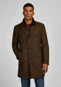 Brauner Fischgrätenmantel mit drei Knöpfen, Reverskragen und seitlichen Taschen, über einem schwarzen Reißverschlussoberteil getragen. Kombiniert mit Jeans.