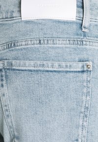 Jeans in denim azzurro leggero con una tasca posteriore, cuciture visibili e un'etichetta bianca in vita. Texture liscia con una finitura sbiadita.