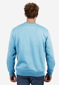 Sudadera azul clara, cuello redondo, mangas largas, textura suave, puños y dobladillo acanalados, detalles minimalistas, combinada con jeans azul oscuro.