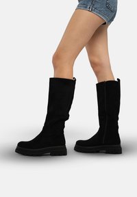 Zwarte suède laarzen tot aan de knie met een stevige zwarte zool en een rits aan de zijkant. Het ontwerp is gestroomlijnd met een comfortabele pasvorm voor de hele dag draagplezier.