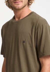 Olive green cotton t-shirt featuring a crew neckline and short sleeves. Left chest has a small black logo. Smooth texture.