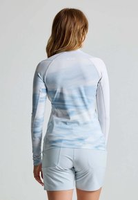 Langärmliges Sportoberteil in Hellgrau und Blau mit wolkenähnlichem Muster, kombiniert mit hellgrauen Shorts. Glattes, strukturiertes Gewebe.
