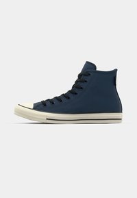 Hoge sneakers in marineblauwe canvas met zwarte veters, witte rubberen neuskap en gestreepte zool. Glad textuur, minimale branding.