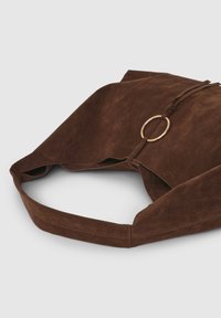 Borsa a tracolla in pelle scamosciata marrone con un grande elemento circolare in metallo dorato, tracolla piatta e texture morbida con un design non strutturato.