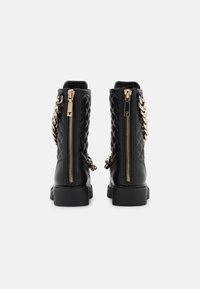 Stivali alla caviglia in pelle nera trapuntata con chiusure a zip dorate e un accento a catena sul lato. Sole in gomma piatta, design in stile militare.