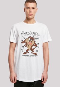 Hvit bomull T-skjorte med "The Tasmanian Devil" grafikk i brun og svart, samt lekne tekstelementer. Korte ermer, rund hals.