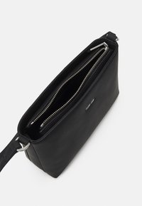 Svart läder crossbody-väska med två dragkedjefack, silverfärgade detaljer och en texturerad yta. Varumärket finns på sidan.
