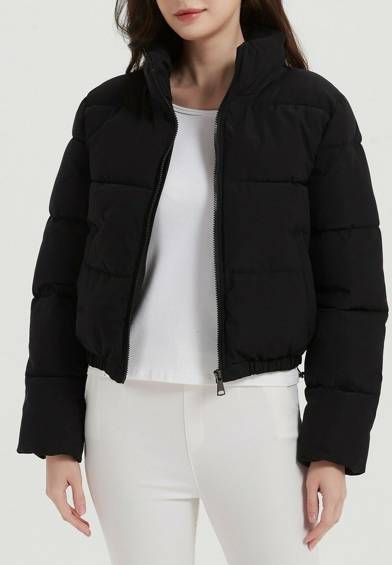 Veste matelassée noire avec un col haut, fermeture éclair à l'avant et ourlet élastique. Dispose de manches larges et d'une texture de tissu lisse et brillant.