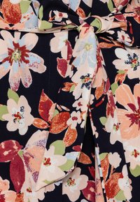 Zbliżenie na tkaninę o granatowym tle z dużym kwiatowym wzorem w odcieniach różu, rdzy, zieleni i jasnoniebieskiego, z wiązanym węzłem jako detalem.