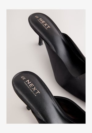 Zwarte slingback pumps gemaakt van glad synthetisch materiaal met een puntige neus en een bescheiden hak. Voorzien van merkemblemen in contrasterende gouden letters op de binnenzool.