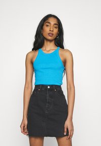 Top de alças largas em malha ribbed azul, combinado com uma saia de ganga preta de cintura alta com fecho de botão e bainha desfiada.