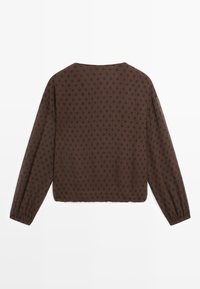 Braune Bluse mit langen Ärmeln und schwarzen Punkten, rundem Ausschnitt und gerafften Bündchen, flach auf einem weißen Hintergrund gelegt.