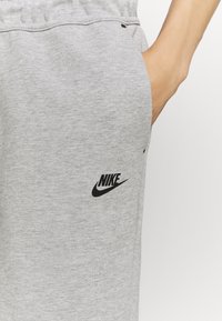 Šedé bavlněné tepláky s černým logem Nike, elastickým pasem a boční kapsou. Hladká textura a pohodlný střih.