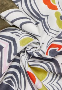 Tessuto stampato con audaci motivi floreali e onde multicolore su uno sfondo bianco. Texture liscia con una sottile lucentezza.