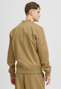 Khaki bomberjack met een gestructureerde pasvorm, ribbelmanchetten en -zoom, en een gladde textuur. Van achteraf weergegeven met een strak ontwerp.