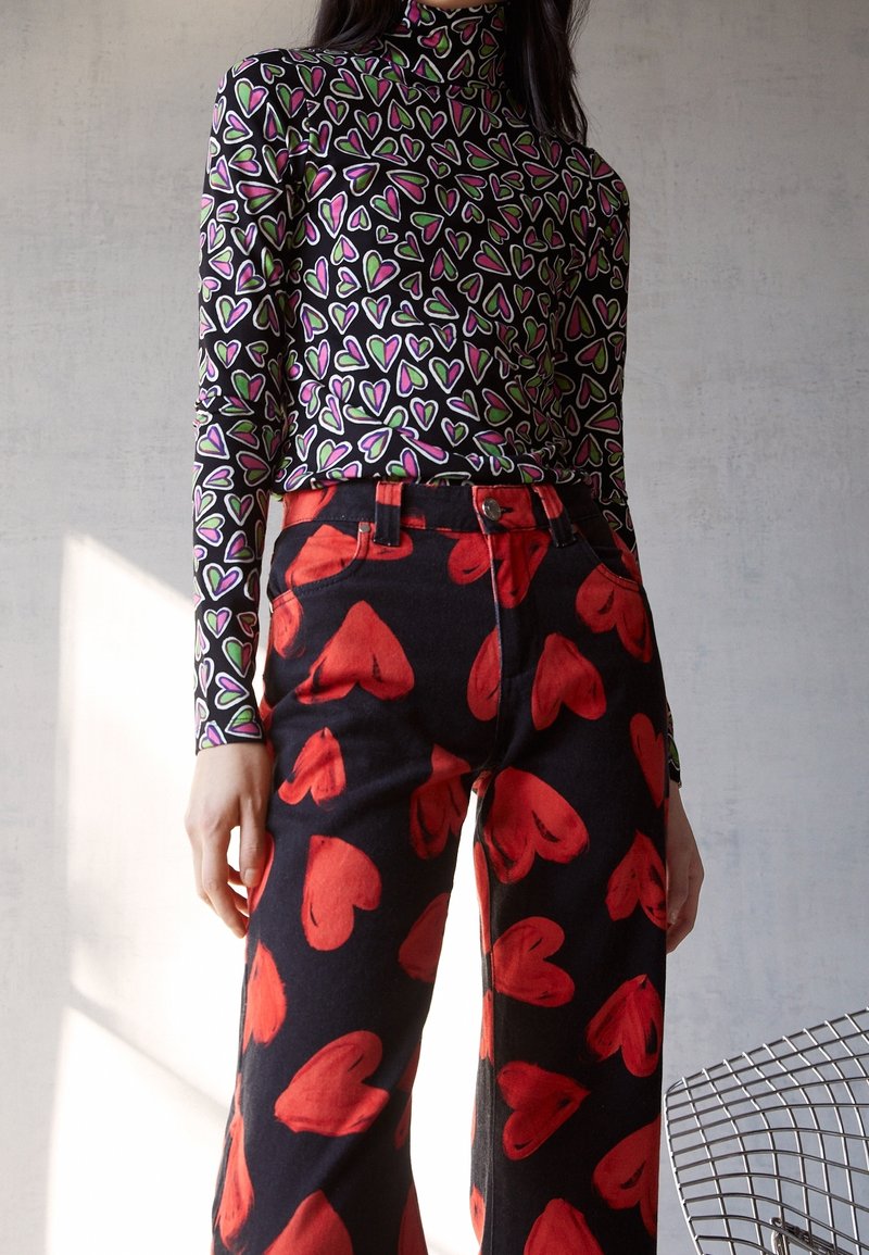Svart polokrage topp med flerfärgade hjärtmönster, parat med högmidjade svarta jeans med stora röda hjärttryck.