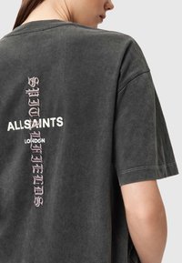 Mørkegrå oversized t-shirt med en syet detalje, med hvid og lyserød tekst på ryggen, hvor der står "ALLSAINTS LONDON" og "FIELDS."