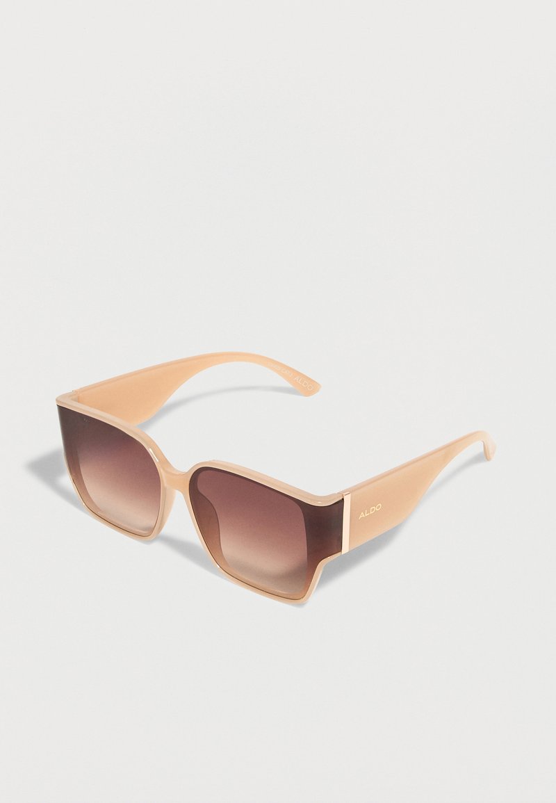 Lunettes de soleil à monture carrée beige avec des verres dégradés marron et des branches larges, marquées ALDO sur la branche.