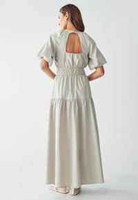 Robe maxi gris clair avec manches bouffantes, taille élastique, découpe au dos et ourlet en couches. Fabriquée à partir d'un tissu lisse.