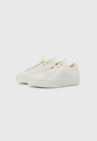 Baskets en cuir blanc avec une texture lisse, présentant des œillets dorés, des lacets blancs et des clous décoratifs blancs sur le talon.