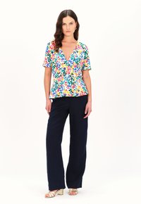 Top envolvente con estampado floral en tonos coloridos y mangas cortas, combinado con pantalones de pierna ancha en color navy y sandalias doradas de tacón bloque.