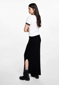 Bílý top s krátkými rukávy a černým lemem v kombinaci s dlouhou černou sukní s bočním rozparkem. Modelka má na sobě černé boty a šedé ponožky.