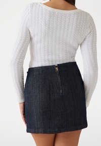 Pull en tricot blanc à texture côtelée et à manches longues, associé à une mini-jupe en jean foncé avec une fermeture éclair centrale.