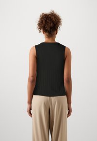 Must mustriba säärisega must tank-top ümarate kaelustega ja ilma varrukateta, kombineeritud beežide laiade pükstega. Sile tekstuur, hästi istuv siluett.