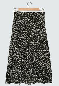 Jupe midi noire à motif floral blanc suspendue sur un cintre en bois avec des pinces en métal, sur un fond clair.