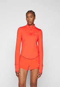 Helderrode sportoutfit bestaande uit een langemouwtop met rits en bijpassende shorts, gemaakt van lichtgewicht, gladde stof met een getailleerd ontwerp.