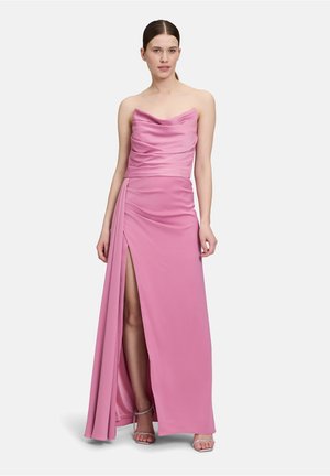Trägerloses pinkes Kleid aus gerafftem strukturiertem Stoff, mit seitlichem Schlitz und fließender Silhouette. Kombiniert mit glitzernden Riemchen-Absatzschuhen.