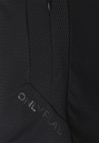 Svart nätmaterial med en texturerad yta, med en dragkedja och den präglade texten "ONLY PLAY" i nedre vänstra hörnet.