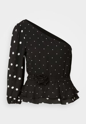 Black blouse with white polka dots, one long sleeve, ruffled peplum hem, and a flower accent at the waist, made of lightweight fabric.