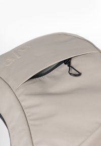 Borsa di stoffa grigia a forma arrotondata, con una tasca con zip dotata di una zip nera e un logo impresso. Texture liscia con una finitura opaca.