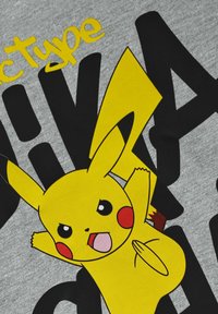 T-shirt grigio in cotone con una grande grafica di Pikachu gialla, accompagnata dalla scritta nera "Pikatype". La texture visibile del tessuto valorizza il design.