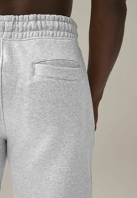 Graue Sweatpants mit einem elastischen Bund, ausgestattet mit einer Gesäßtasche und weichem, strukturiertem Stoff. Nahaufnahme der Rückseite und Seite.
