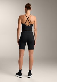 Fekete sportos tank top keresztezett pántokkal és illő, magas derékú kerékpáros shorttal. Sima, ruganyos anyag; minimalista dizájn.